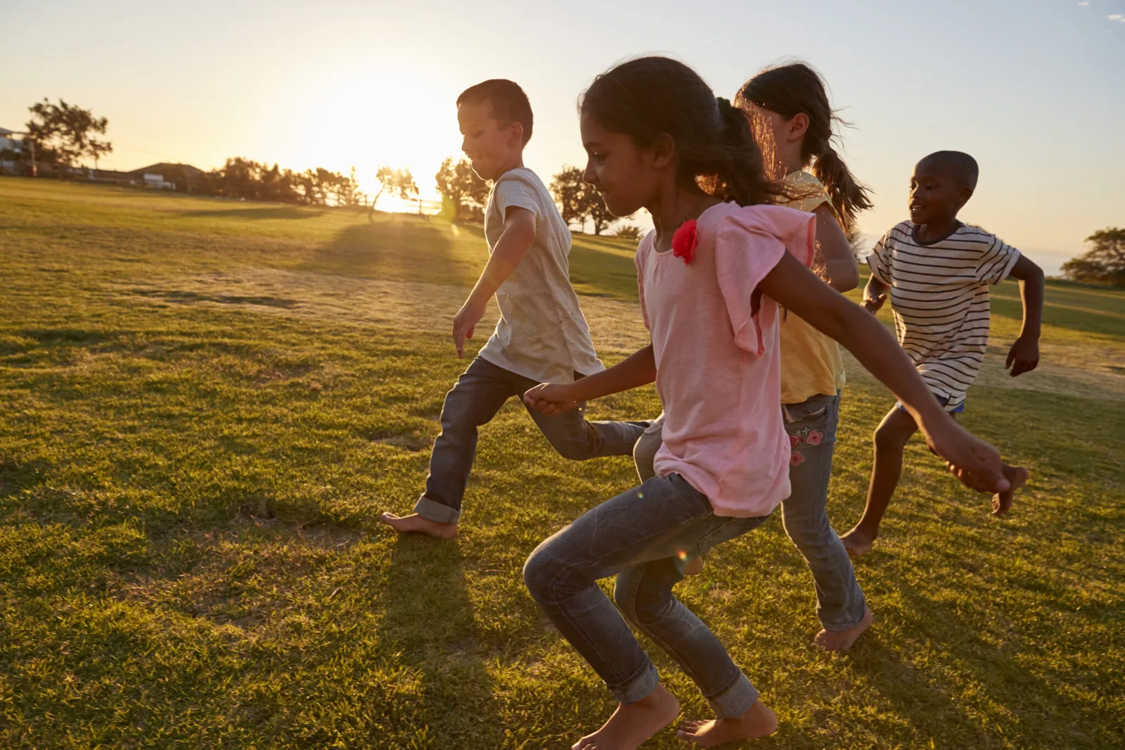 Children running barefoot across a park at sunset
