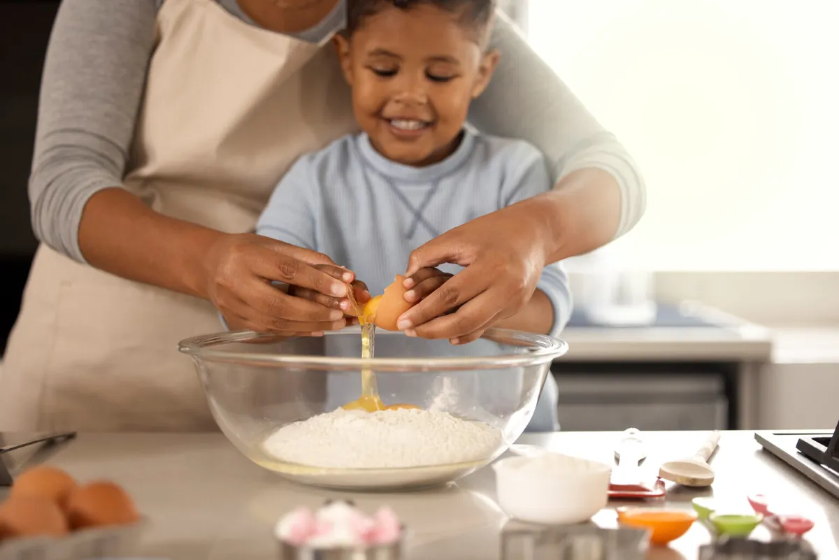 A parent and child cracking eggs into a mixing bowl