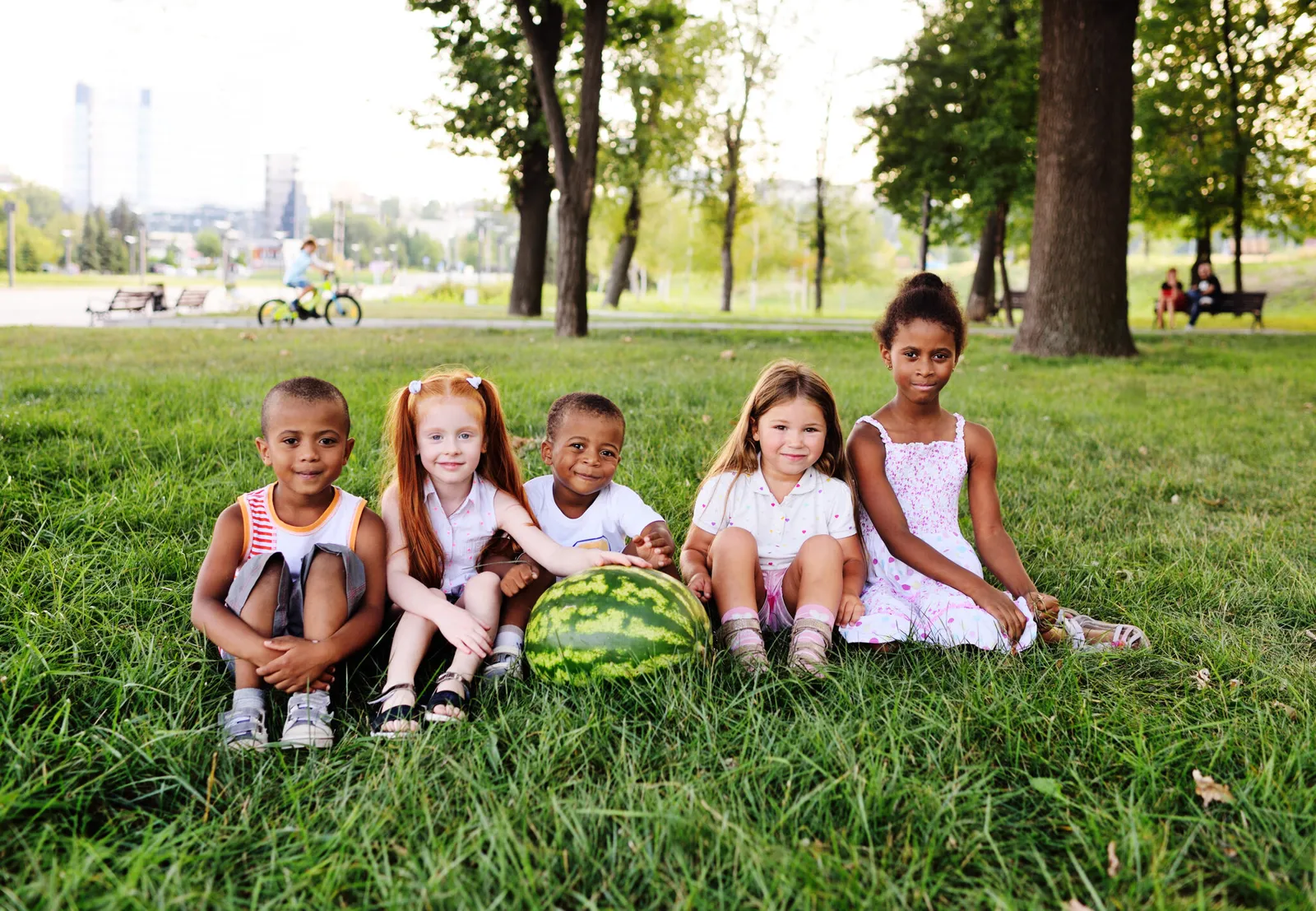 Five young children sitting together on the grass in a park